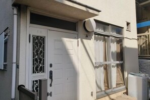 A white door with a decorative glass panel, a window with blinds, and a white outdoor unit on the wall.