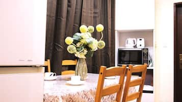 Un comedor con una mesa lista para dos personas, un jarrón con flores y un microondas al fondo.