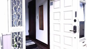 A white door with a traditional design, a small set of stairs leading to a dark wooden door, and a window with a decorative metal grille. - Tokyo Yoshimi home stay (Tokyo)
