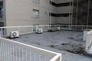 An outdoor rooftop area with multiple air conditioning units, a white railing, and a building with multiple floors and windows. - Tokyo Yoshimi home stay (Tokyo)