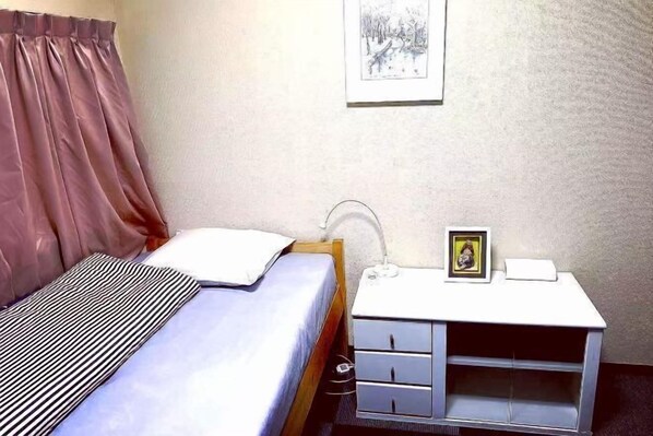 A bedroom with a bed, a bedside table with drawers, a framed picture, and a window with curtains. - Tokyo Yoshimi home stay (Tokyo)