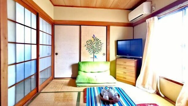 A traditional Japanese room with tatami flooring, a futon bed, a television, and sliding doors. - Tokyo Yoshimi home stay (Tokyo)