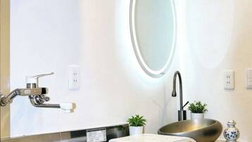 A modern bathroom with a large mirror, a sink with a vessel basin, a scale, and a small potted plant.