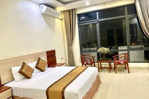 Ein Hotelzimmer mit Bett, Tisch mit Stühlen, einem Fenster mit Vorhängen und einer Klimaanlage.