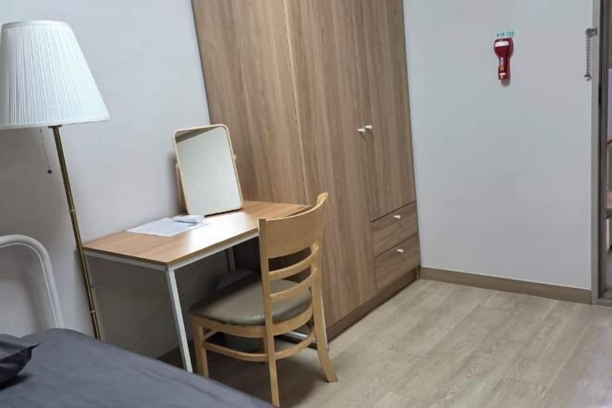 A bedroom with a bed, a desk with a chair, a wardrobe, and a lamp.
