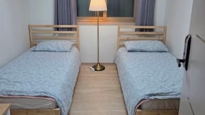 A twin room with two single beds, a bedside table, a floor lamp, and a window with curtains. - EDEN GUEST HOUSE (Seoul)