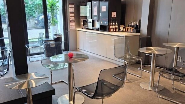 A modern cafe with glass tables and chairs, a counter with beverages, and a view of the street. - EDEN GUEST HOUSE (Seoul)