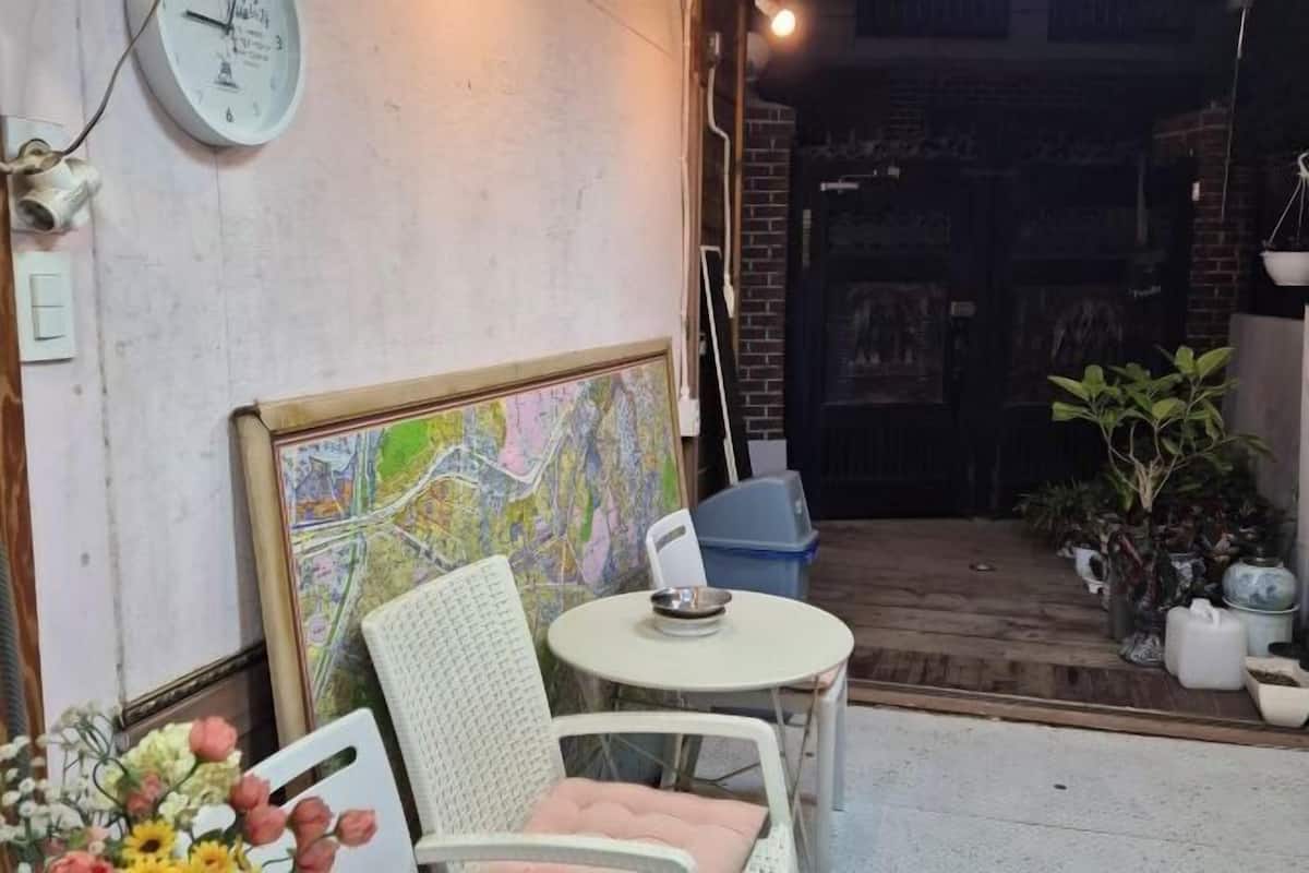 A room with a map on the wall, a clock, a round table with a chair, and potted plants.