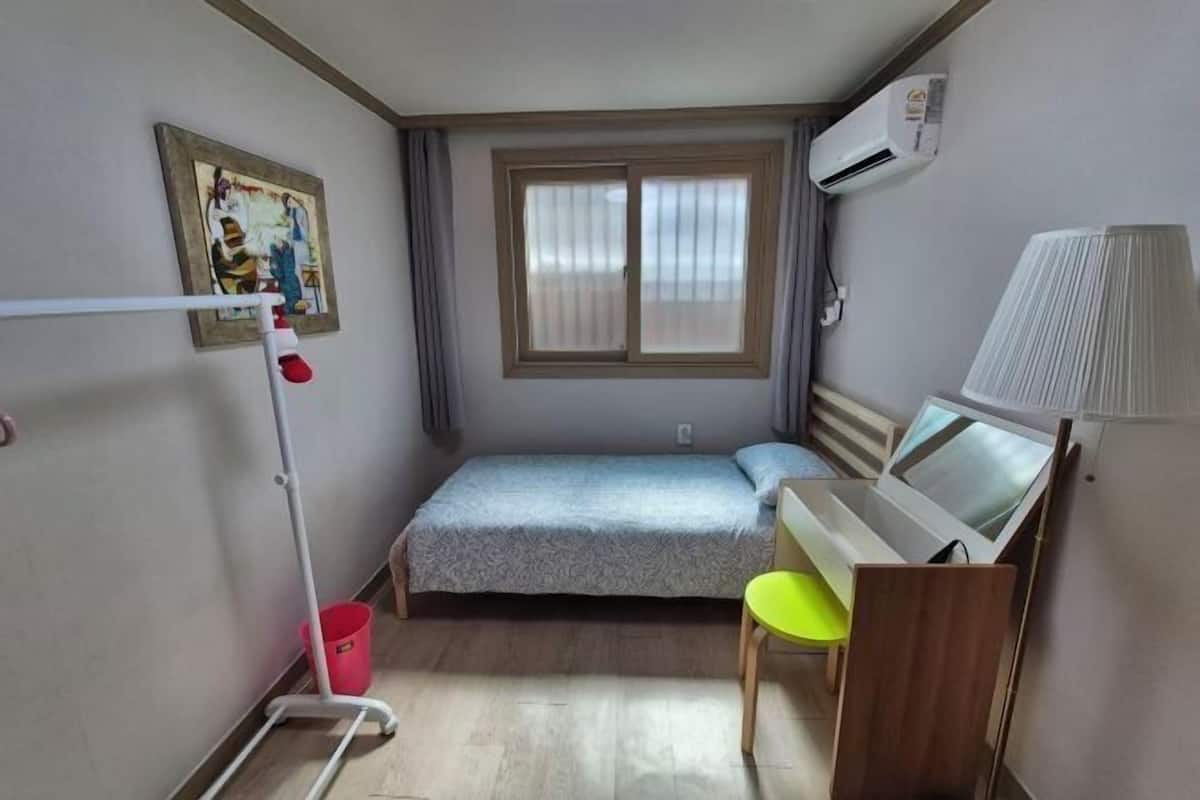 A small room with a bed, a desk, a chair, a window, and an air conditioning unit.