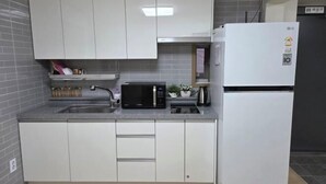 A compact kitchen with white cabinets, a microwave, a refrigerator, and a sink. - EDEN GUEST HOUSE (Seoul)