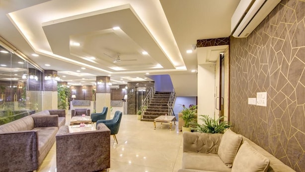 Un vestíbulo amplio con un diseño moderno, que incluye una zona de estar con sofás y sillones, una escalera y una pared de vidrio con vistas al exterior.