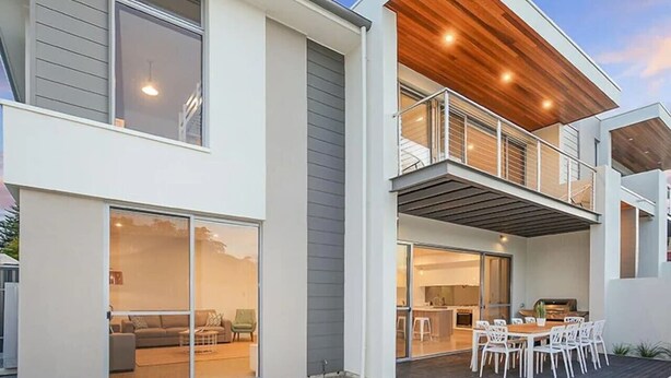 Ein modernes, zweistöckiges Haus mit Balkon, großen Schiebegläsern und einer Terrassenfläche.