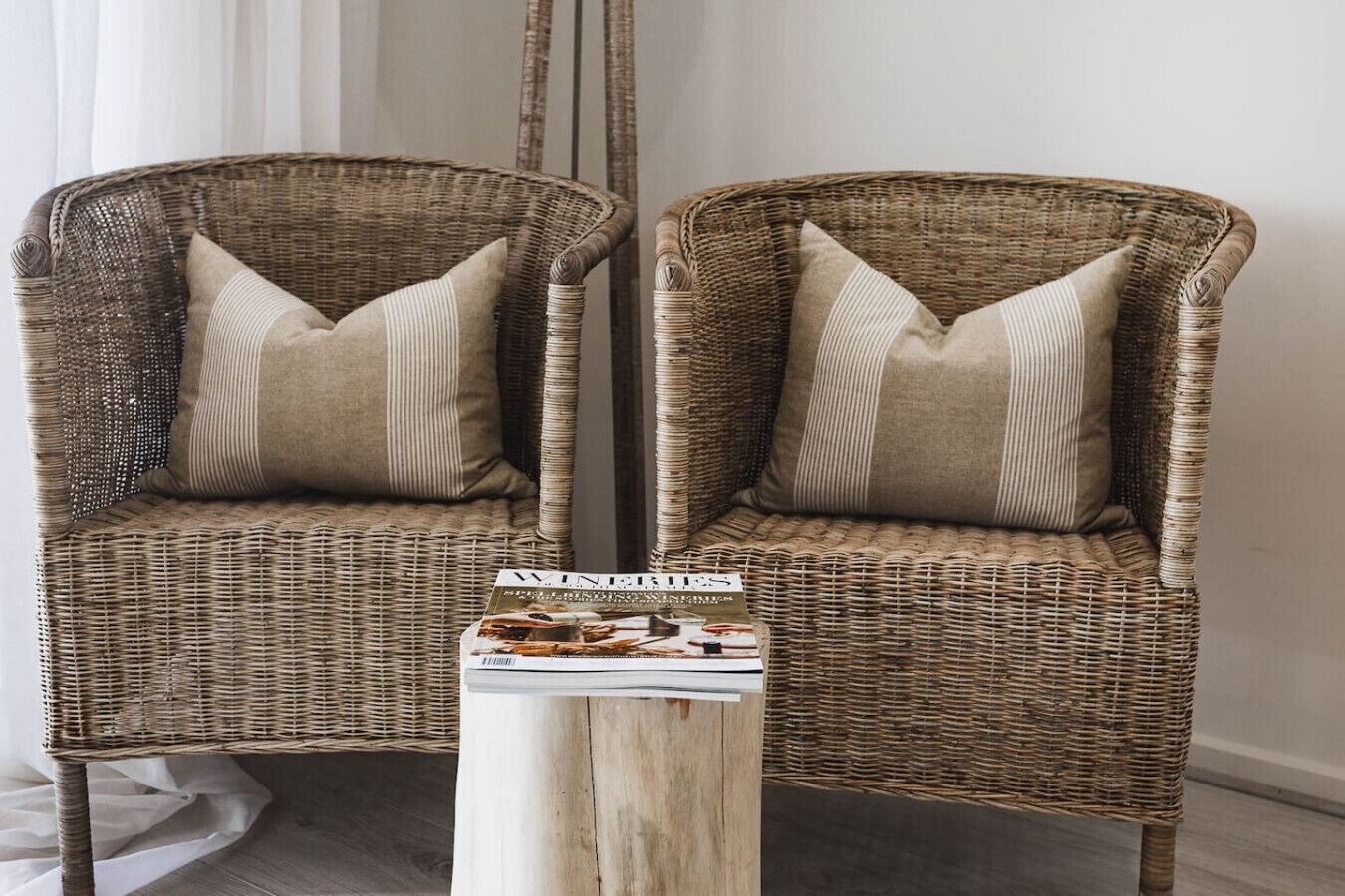 Two wicker chairs with matching cushions, a wooden side table with a magazine, and a plain wall in the background.