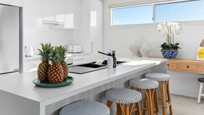 Una cocina moderna con muebles blancos, una isla grande con taburetes, un tostador y una piña sobre la encimera.