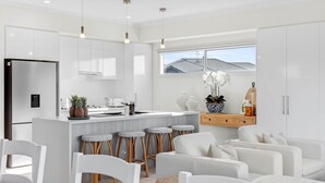 Una cocina moderna con armarios blancos, una isla central con taburetes altos y vistas al exterior a través de un gran ventanal.
