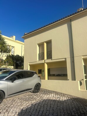 Un bâtiment à deux étages, avec un toit recouvert de tuiles, une voiture garée et une allée pavée.