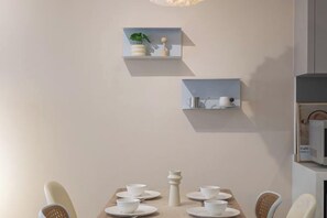 Un comedor con una mesa dispuesta para cuatro personas, dos estantes fijos en la pared con adornos, y un microondas sobre un mueble.