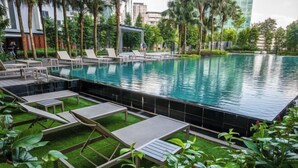 Piscina con sillones de descanso y una pequeña mesa, rodeada de follaje y palmeras.