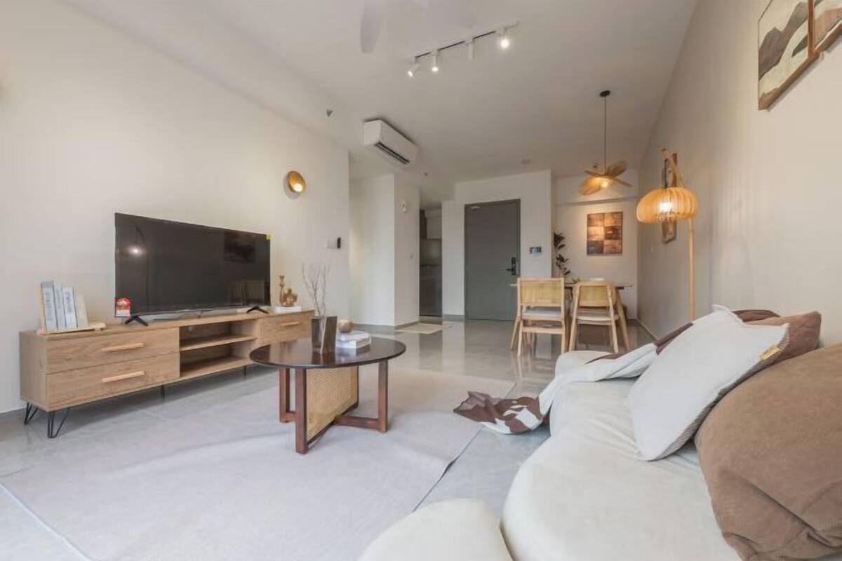 A modern living room with a flat-screen TV, wooden furniture, a round coffee table, and a sofa with cushions.