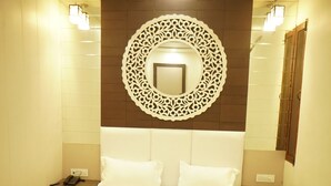 A neatly made bed with a headboard, a wall-mounted decorative mirror, and bedside tables with lamps. - HOTEL SOLUXE (Jagadhri)