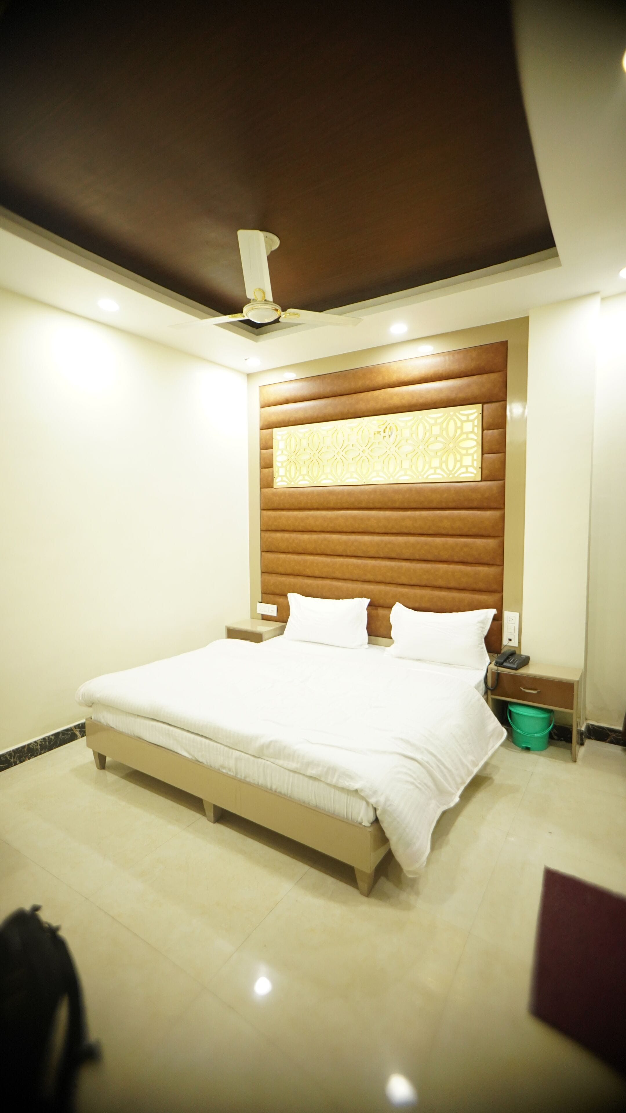 A bedroom with a bed, a nightstand, a green bucket, and a ceiling fan.