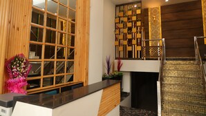 A reception area with a wooden reception desk, a large window with a grid pattern, and a decorative wall with a geometric design. - HOTEL SOLUXE (Jagadhri)