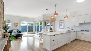 Una cocina moderna con armarios blancos, una isla central, iluminación colgante y vistas al exterior.