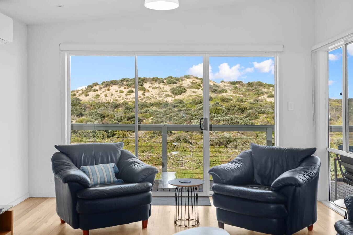 A room with two black leather chairs, a small round table, and a view of a hilly landscape through large glass doors.