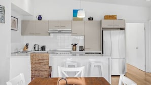 Et moderne køkken med hvide skabe, en central ø med barstole, et køleskab og en hængende lampe.