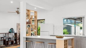 A modern kitchen with a white countertop, wooden bar stools, and built-in shelves. - The Burrow - Pet-friendly Haven near Middleton Beach (Middleton)
