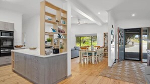 A modern kitchen with grey cabinets, a wooden island, and a dining area with a table and chairs. - The Burrow - Pet-friendly Haven near Middleton Beach (Middleton)