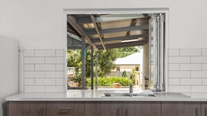 A modern kitchen with a large window, white tiles, and a wooden countertop. - The Burrow - Pet-friendly Haven near Middleton Beach (Middleton)