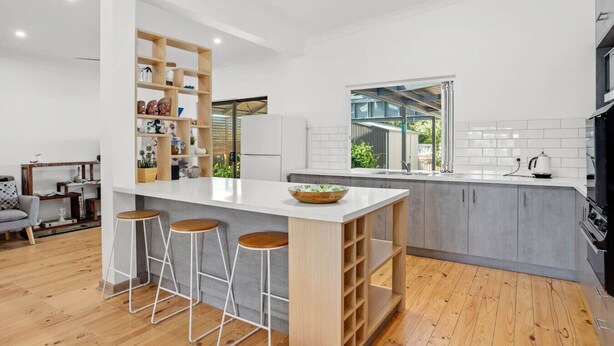 A modern kitchen with a central island, bar stools, and a built-in bookshelf. - The Burrow - Pet-friendly Haven near Middleton Beach (Middleton)