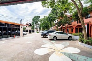 A parking area with cars, a building with a tiled roof, and trees. - Lanna Hotel by Kasalong Resort and Spa Pattaya (Pattaya)