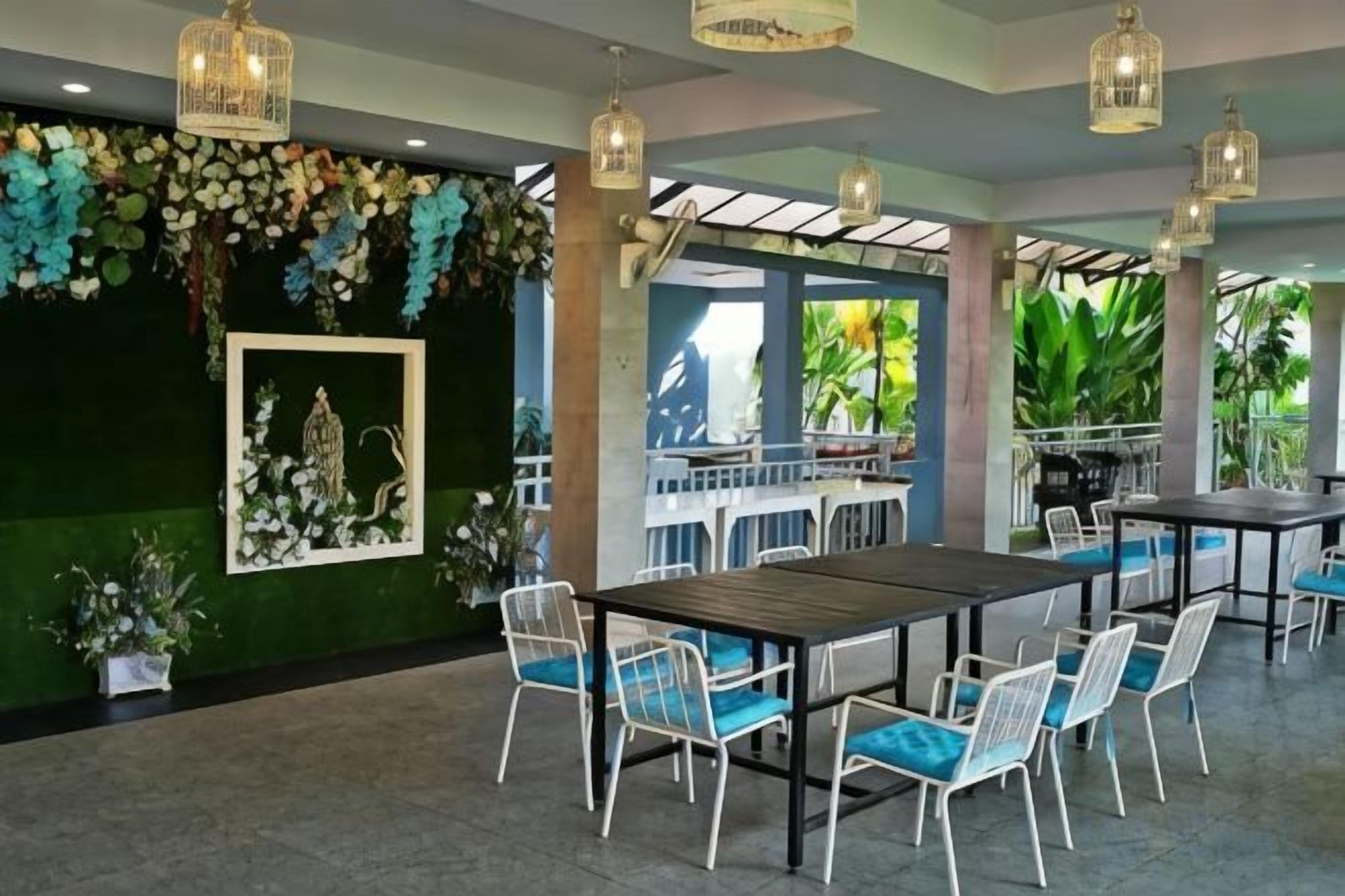 A restaurant with a long table and chairs, a green wall with a framed picture, and hanging lights.