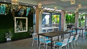 A restaurant with a long table and chairs, a green wall with a framed picture, and hanging lights.