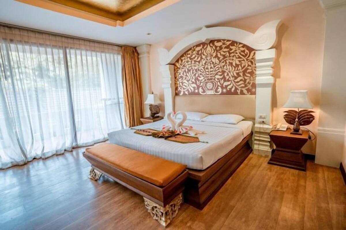 Une chambre d’hôtel avec un grand lit, une banquette, une table de chevet et une fenêtre avec des rideaux.