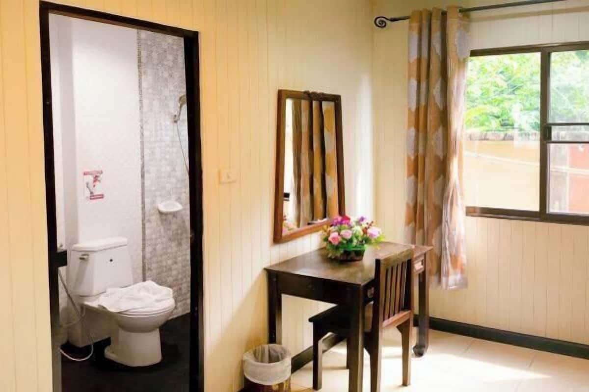 Une salle de bain avec des toilettes, une douche et une petite table sur laquelle est posé un vase de fleurs.