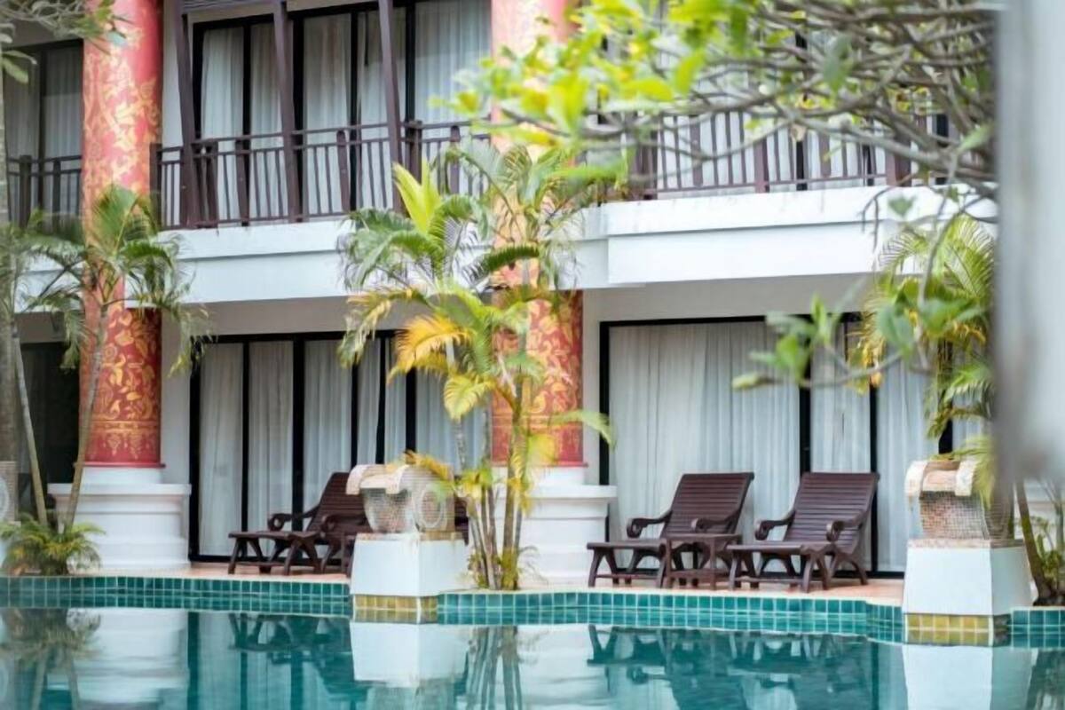 Un hôtel doté d’un espace piscine, avec un bâtiment à deux étages agrémenté de balcons, d’un pilier rouge et de chaises longues.