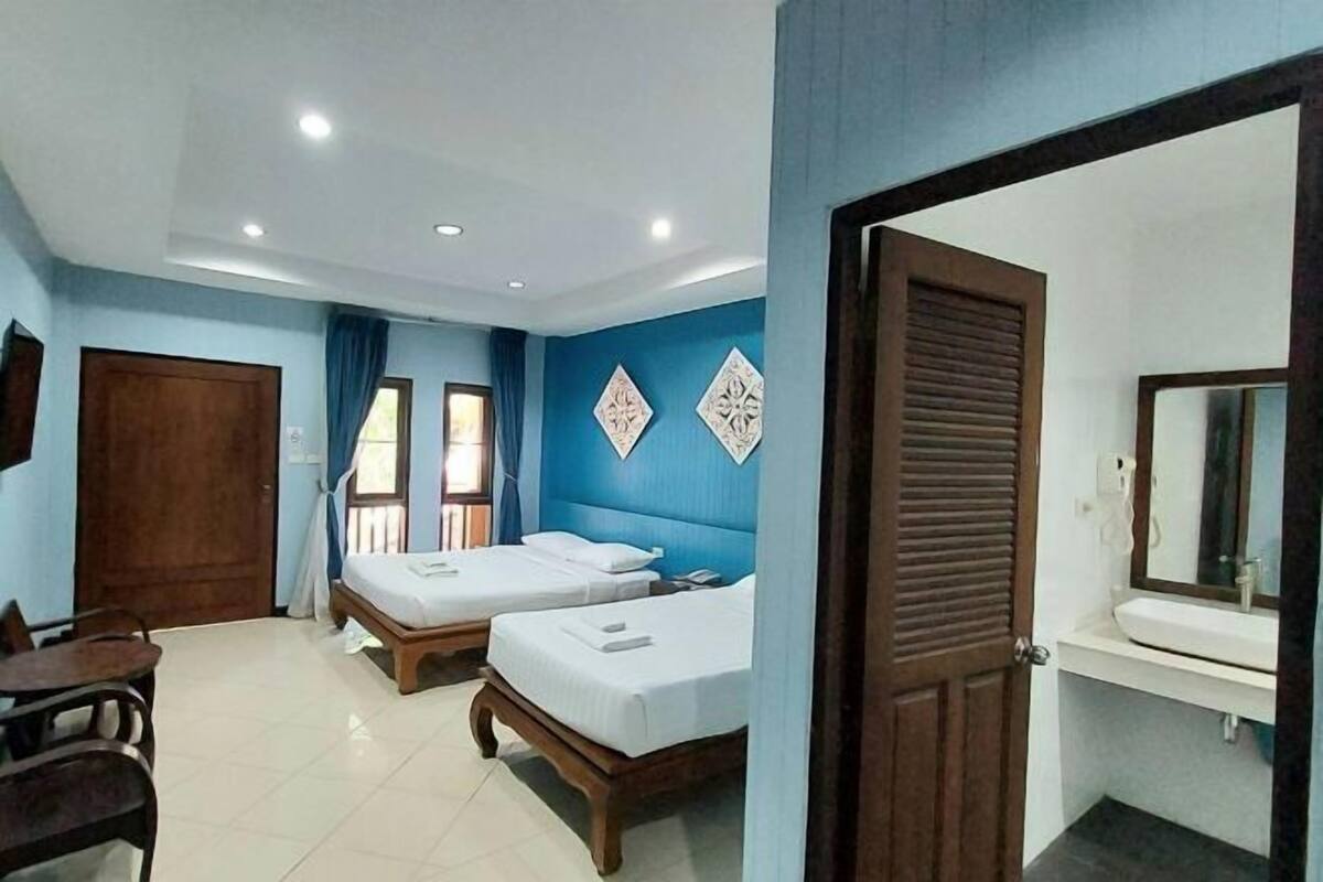 Une chambre d’hôtel avec deux lits, un bureau, une chaise, une salle de bain avec un lavabo et un miroir, et des œuvres d’art décoratives au mur.