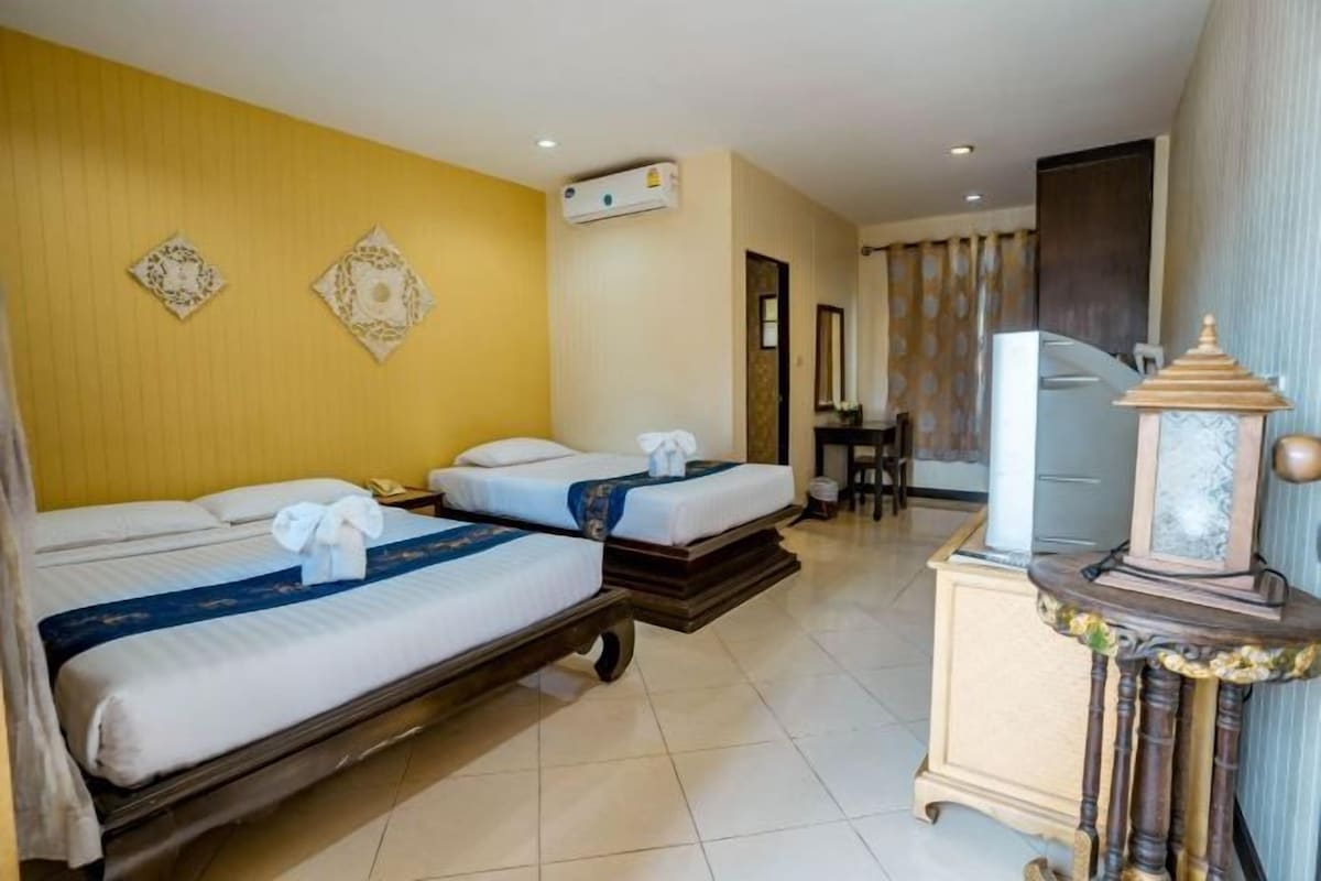 A hotel room with two beds, a desk, a television, and a decorative lamp.