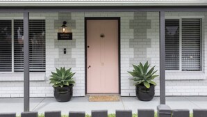 A single-story house with a light-colored brick facade, a beige front door, and two potted plants on either side. - Berechiah Cottage—Stroll to Cafés & Coast (Port Elliot)