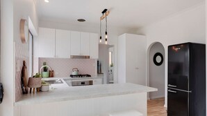 A modern kitchen with white cabinetry, a black refrigerator, and a central island with stools. - Berechiah Cottage—Stroll to Cafés & Coast (Port Elliot)