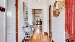 A hallway with wooden floors, a white door on the left, a red door on the right, and a wooden bench with a basket and a bowl. - Red Door Cottage - Heritage Warmth by the Sea (Port Elliot)