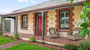 A two-story house with a red door, brick exterior, and a covered porch with wicker furniture. - Red Door Cottage - Heritage Warmth by the Sea (Port Elliot)