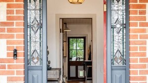 A wooden door with a black frame and glass panels, leading into a room with a tiled floor and a hanging light fixture. - Red Door Cottage - Heritage Warmth by the Sea (Port Elliot)