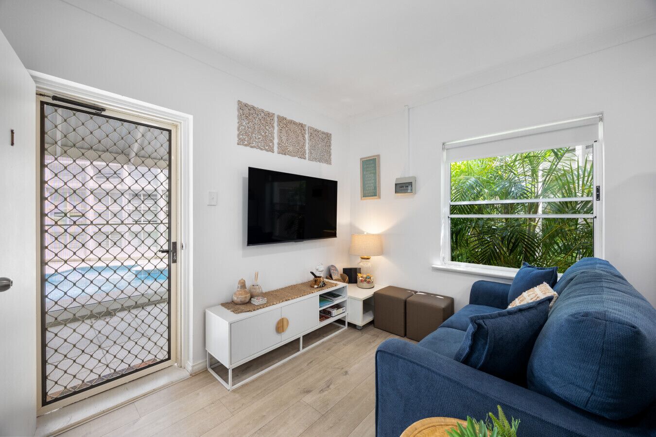 Ein modernes Wohnzimmer mit Fernseher, Sofa und Blick auf einen Pool durch eine Glastür.
