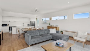 Ein modernes Wohnzimmer mit einem grauen Ecksofa, einem Holztisch und einem Essbereich mit Tisch und Stühlen.