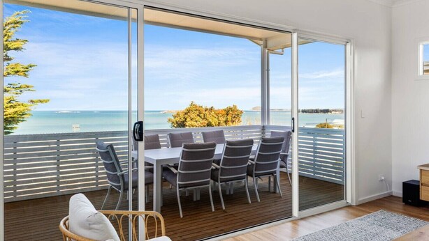 Ein Balkon mit Tisch und Stühlen, ein Korbstuhl und Blick aufs Meer.
