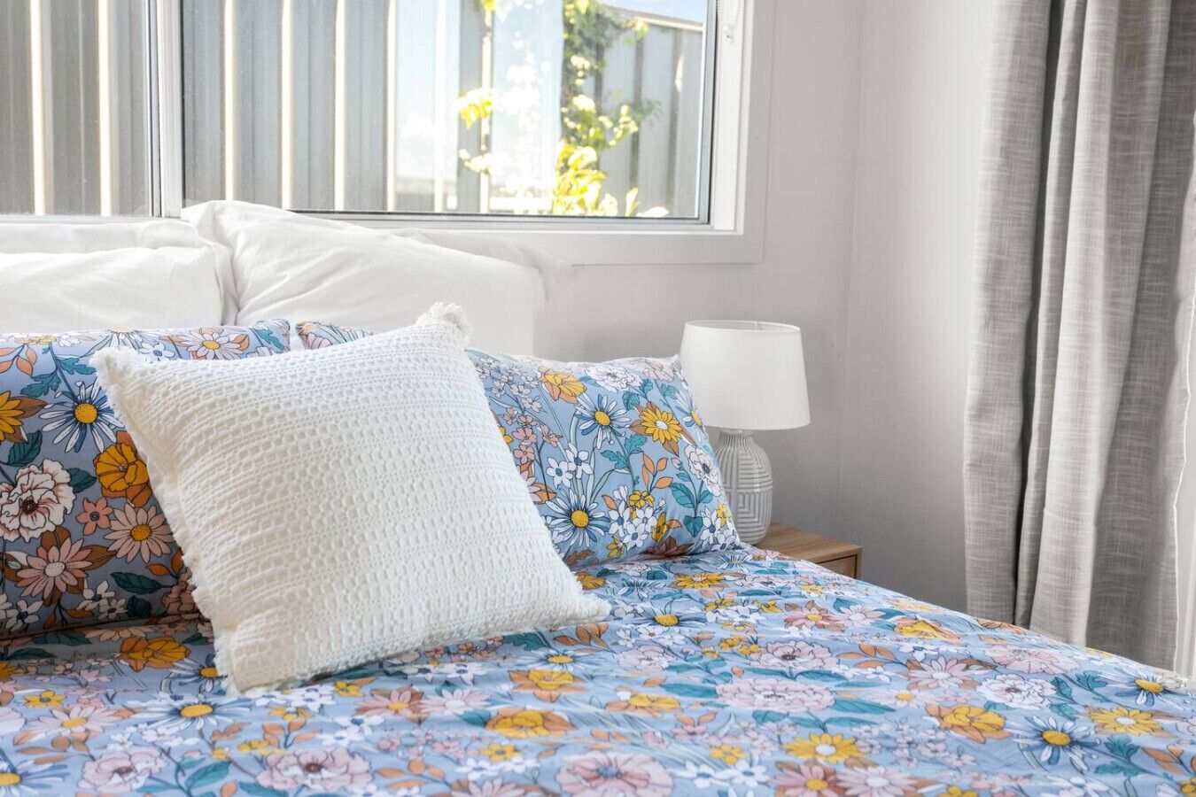 Una cama con una colcha estampada con motivos florales, almohadas blancas y una lámpara de noche.